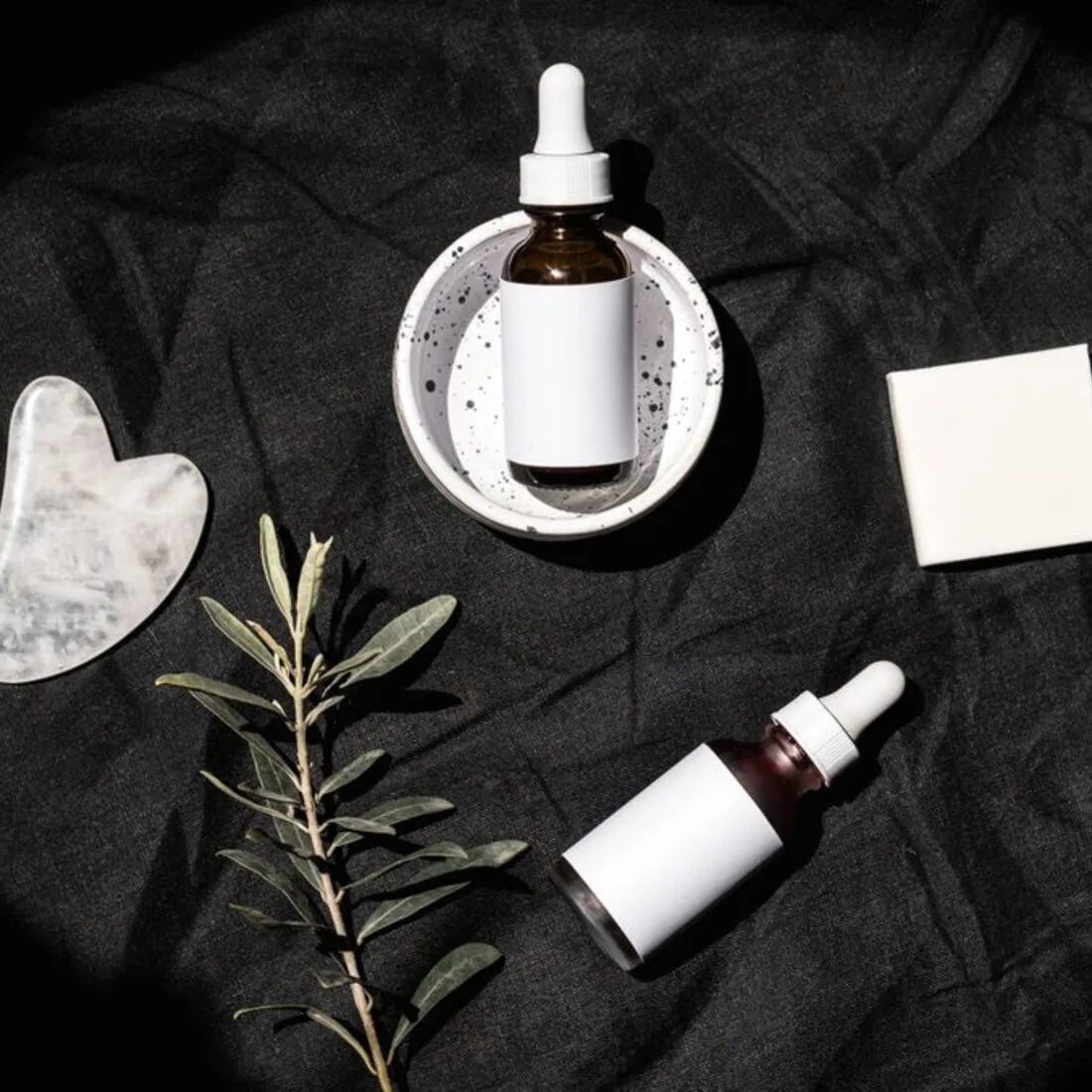 Frasco con gotero y gua sha sobre textil oscuro