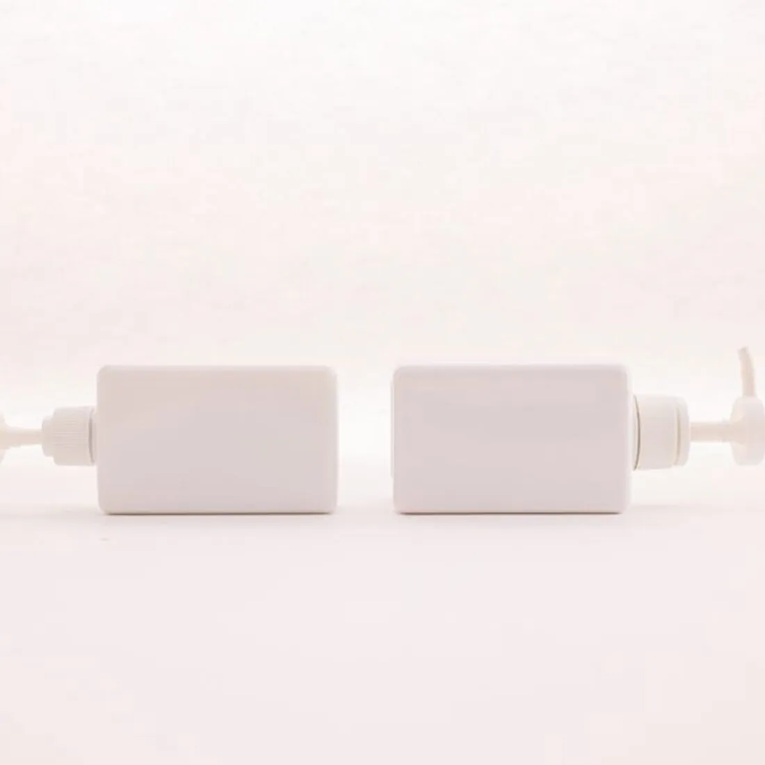 Dos envases blancos de cosmética sobre fondo rosa pálido