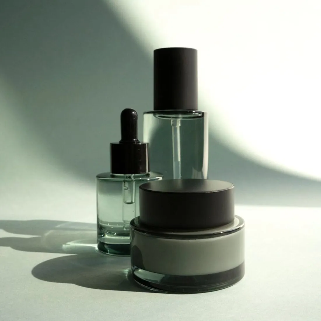 Frascos y tarro de cosmética sobre fondo verde suave